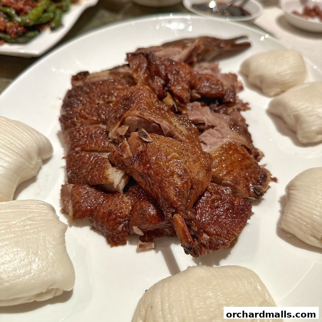A plate of crispy roasted duck served with steamed buns.