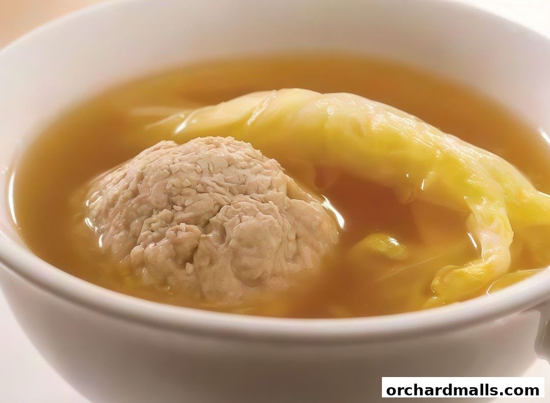 A close-up shot of a steaming bowl of soup with a large meatball and cabbage.