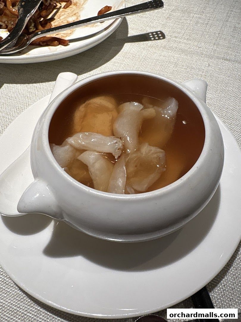A close-up of a delicate soup served in a white ceramic bowl with a spoon.