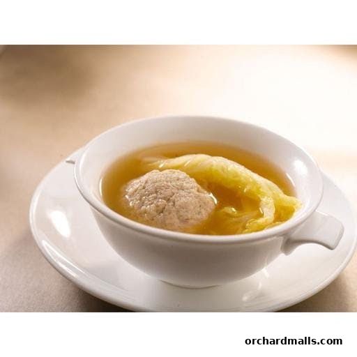 A close-up shot of a steaming bowl of soup with a meatball and cabbage.