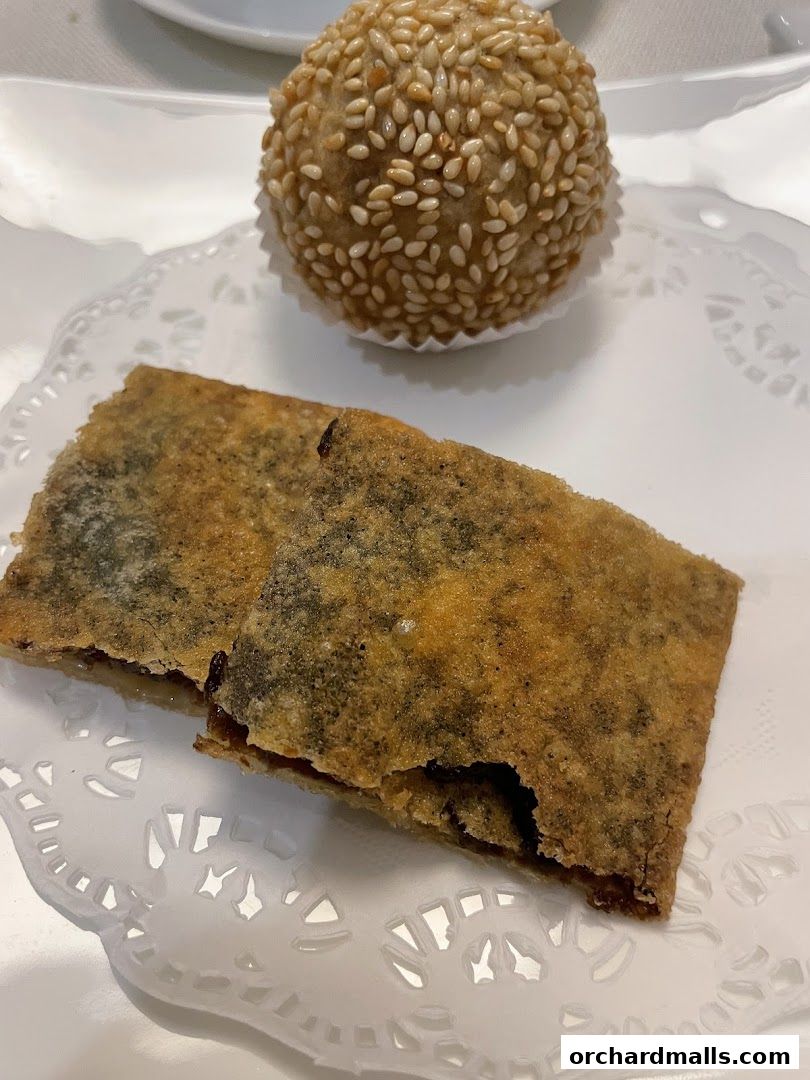 A close-up of two fried Shanghai pastries and a sesame ball on a white doily.