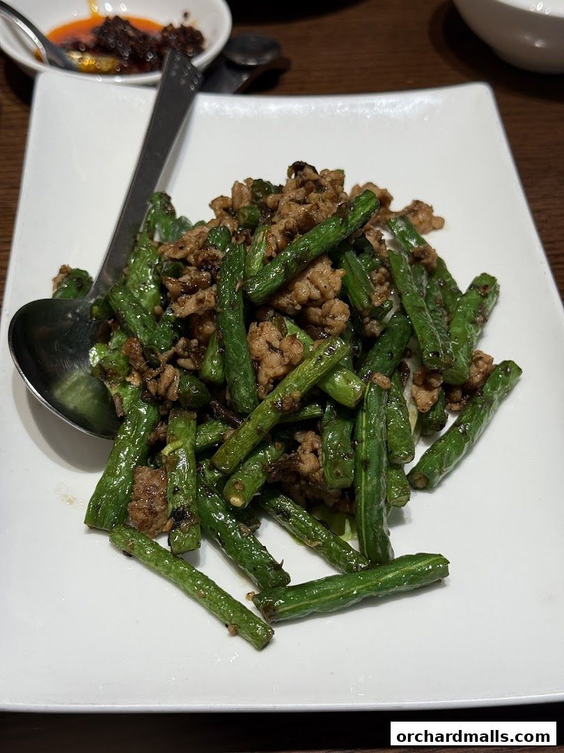 A plate of stir-fried green beans with minced meat, served with a side of chili paste.