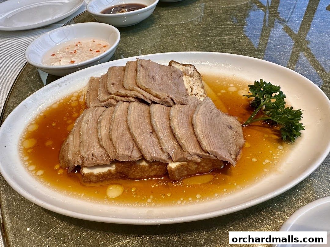 A plate of sliced braised meat served with tofu and a savory sauce, garnished with parsley.