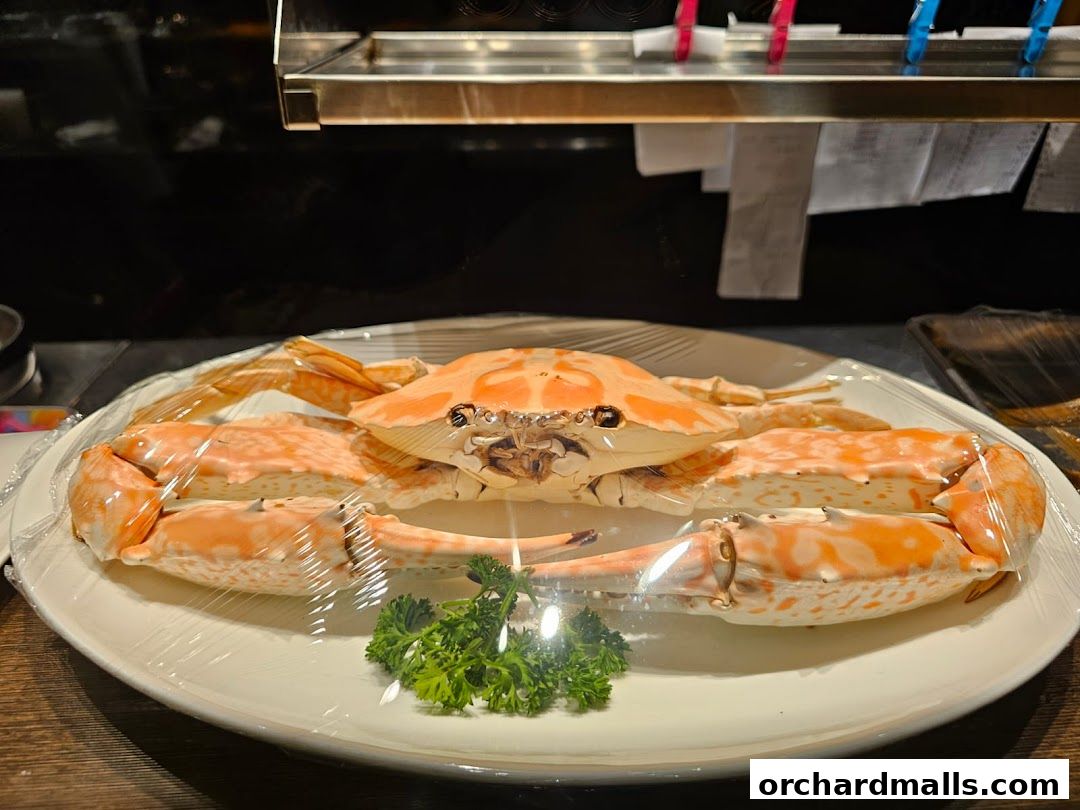A whole cooked crab, garnished with parsley, is presented on a white plate, covered in plastic wrap.