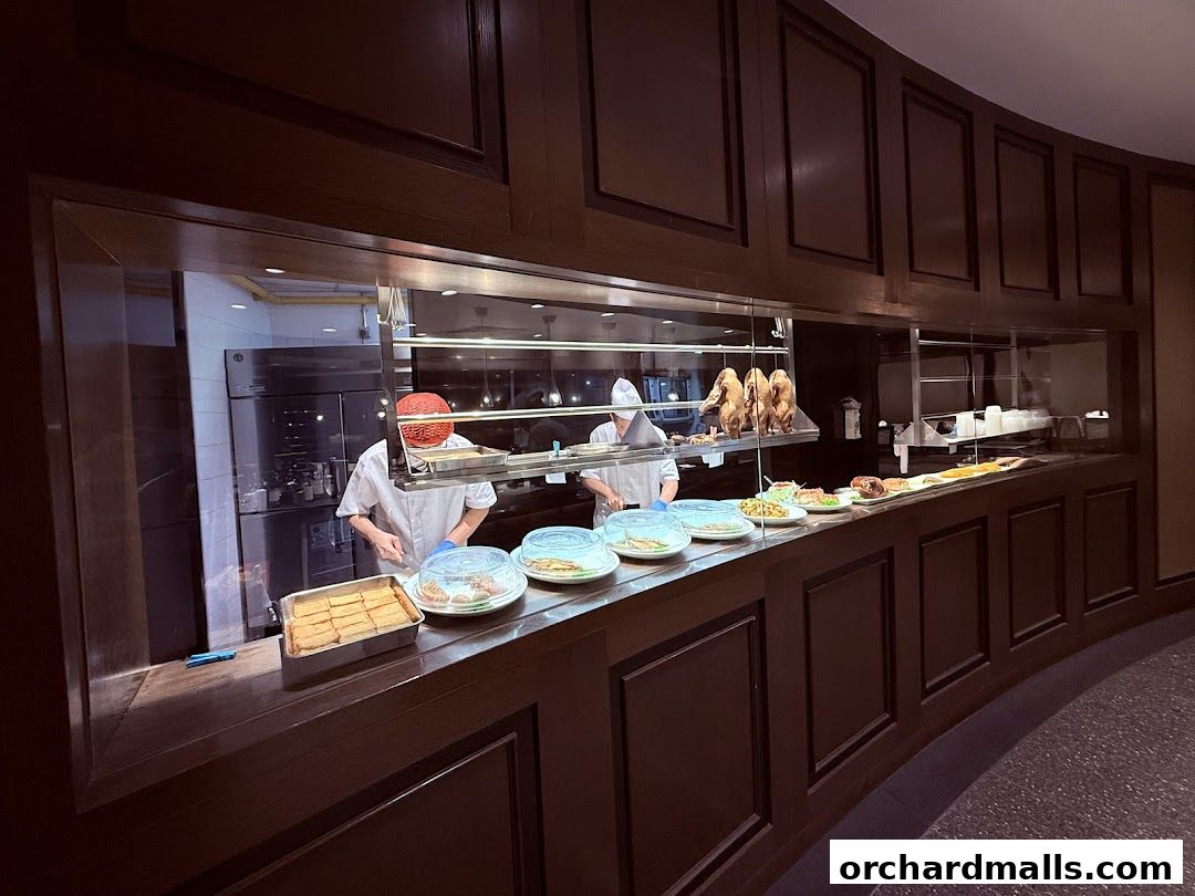 Chefs prepare food behind a counter displaying roasted ducks and various dishes.