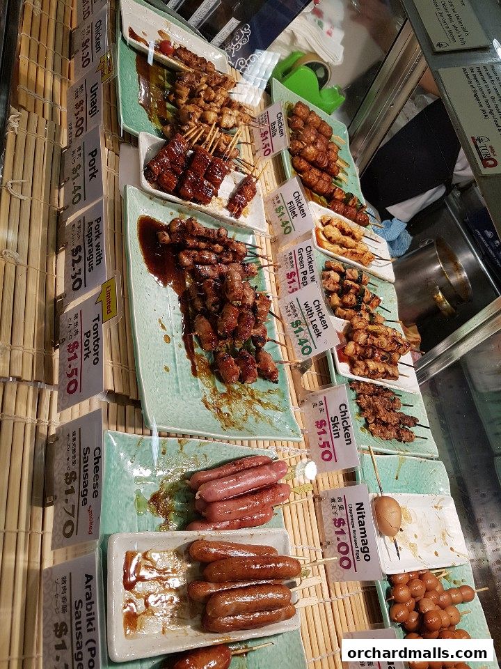 A display of various skewers of grilled meats and sausages with price labels.