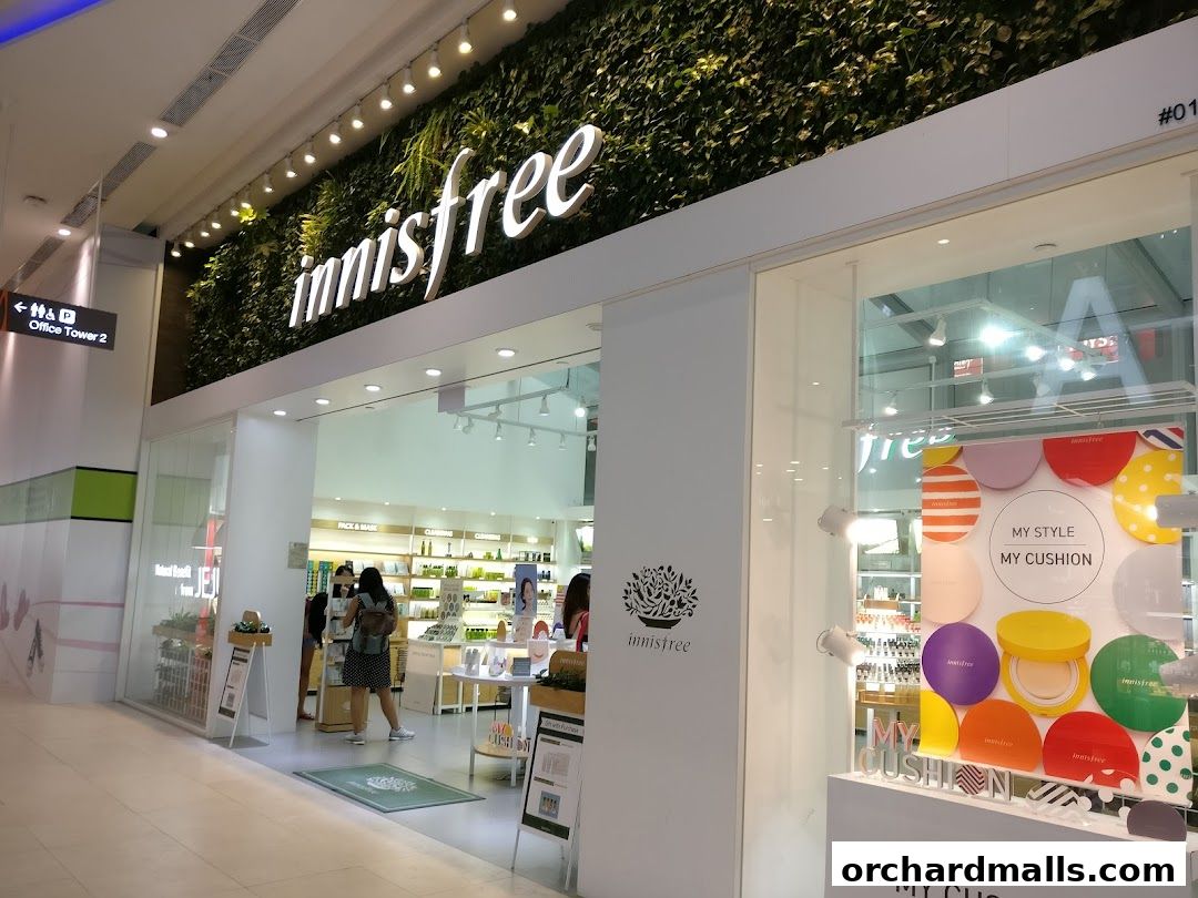Innisfree store entrance with green wall, illuminated logo, and product displays.