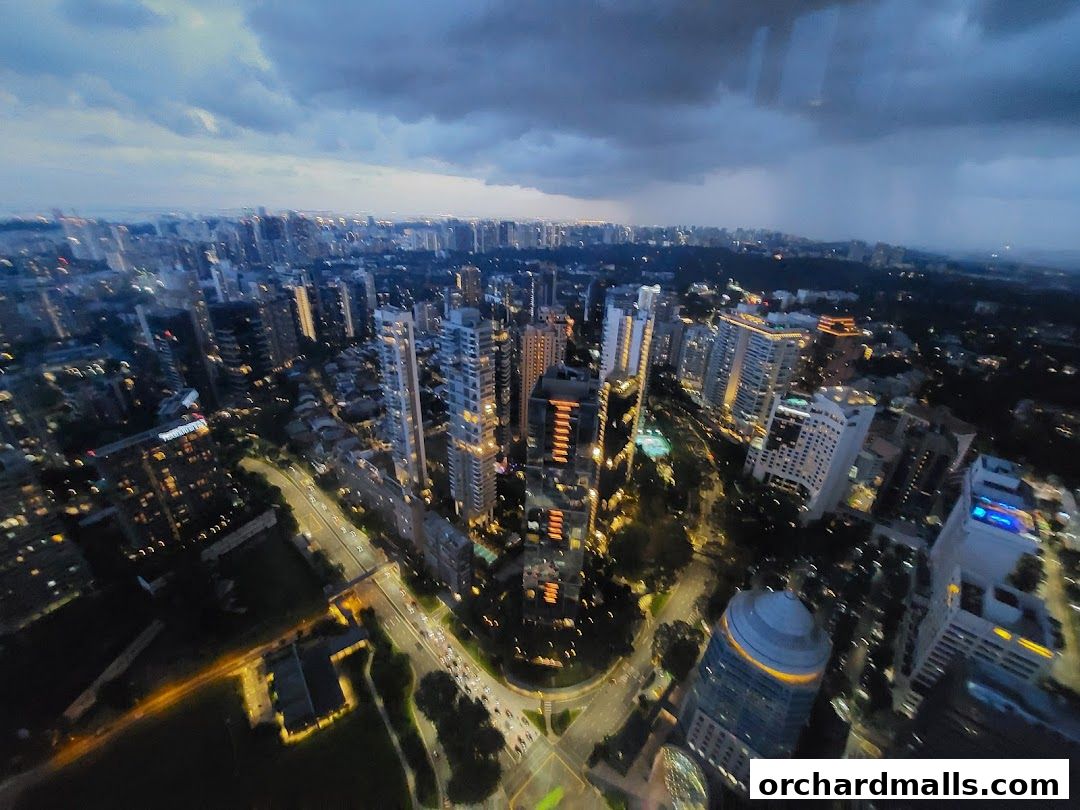 An aerial view of a city skyline at dusk with illuminated buildings and a cloudy sky.
