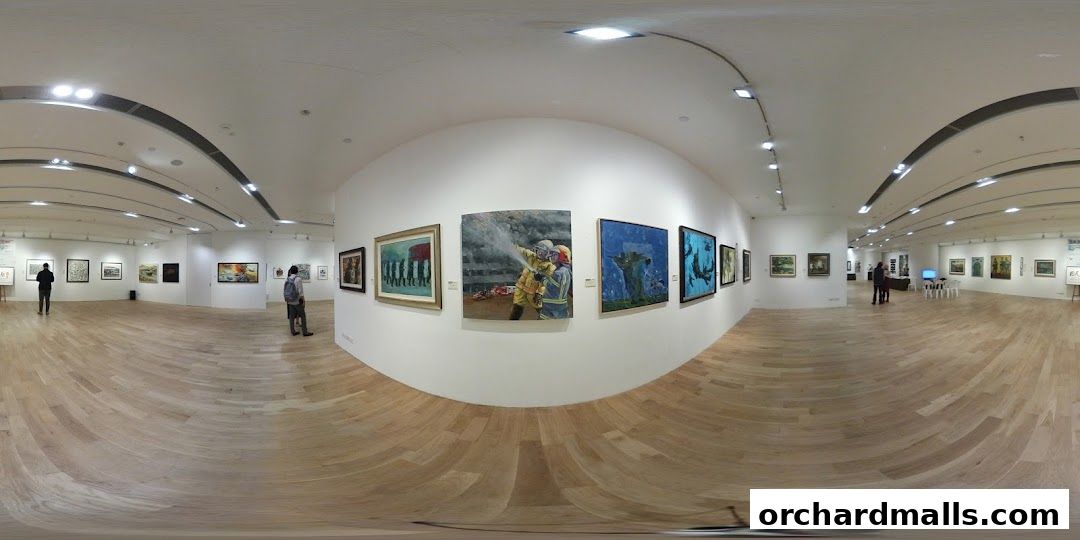 Interior view of an art gallery with various paintings displayed on white walls and wooden floors.
