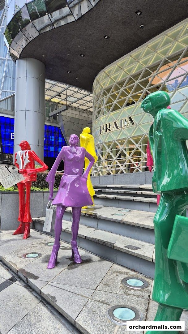 Colorful sculptures of people stand outside a modern building with a Prada store.