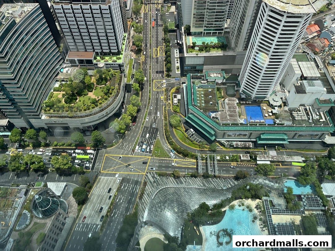 Aerial view of a city intersection with buildings, roads, and greenery.