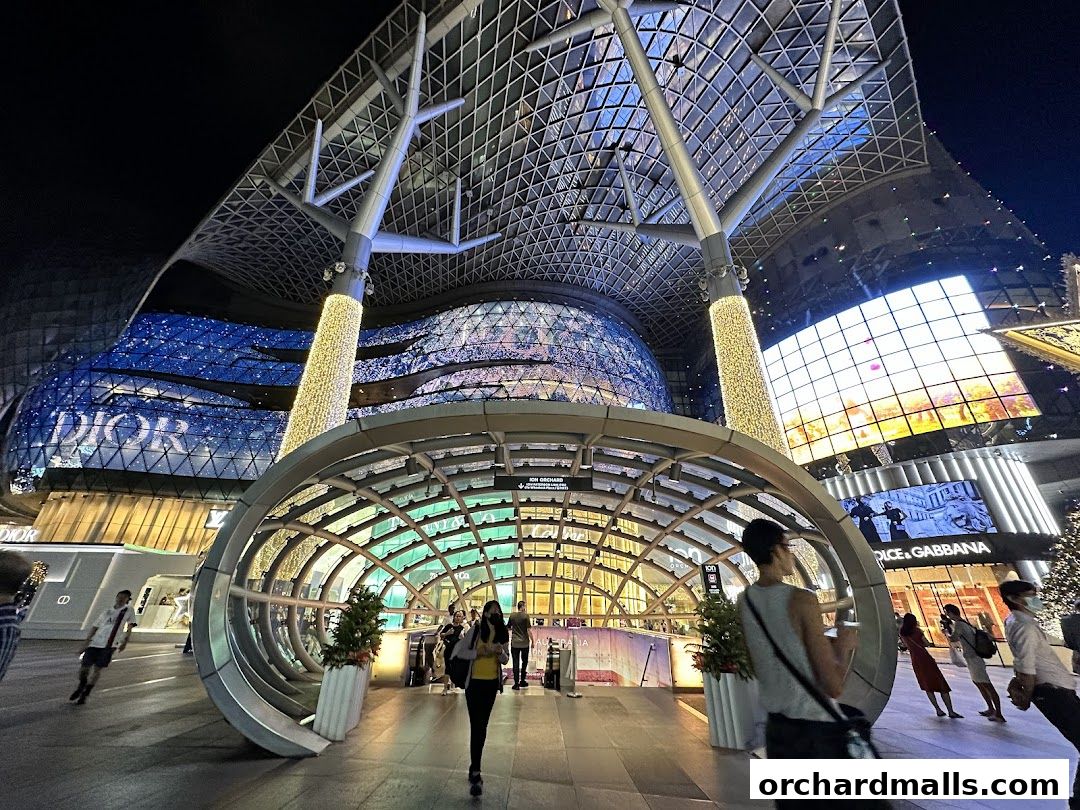 A modern architectural entrance at night with illuminated displays and people walking.