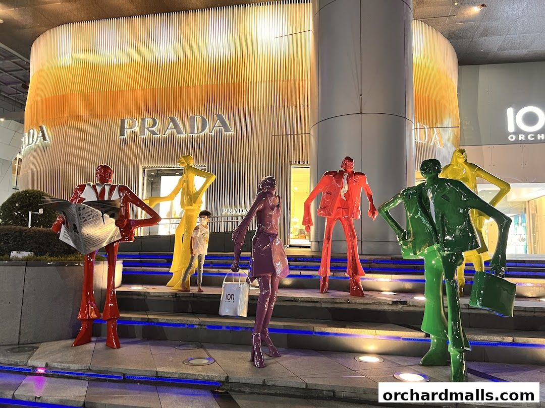 Colorful sculptures of people in suits stand in front of a brightly lit Prada store at night.