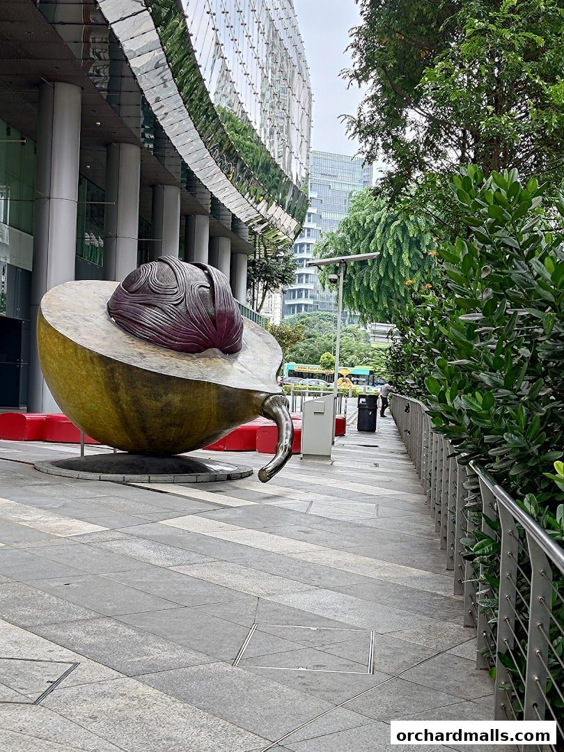 A unique sculpture outside a modern building with a reflective facade and lush greenery.