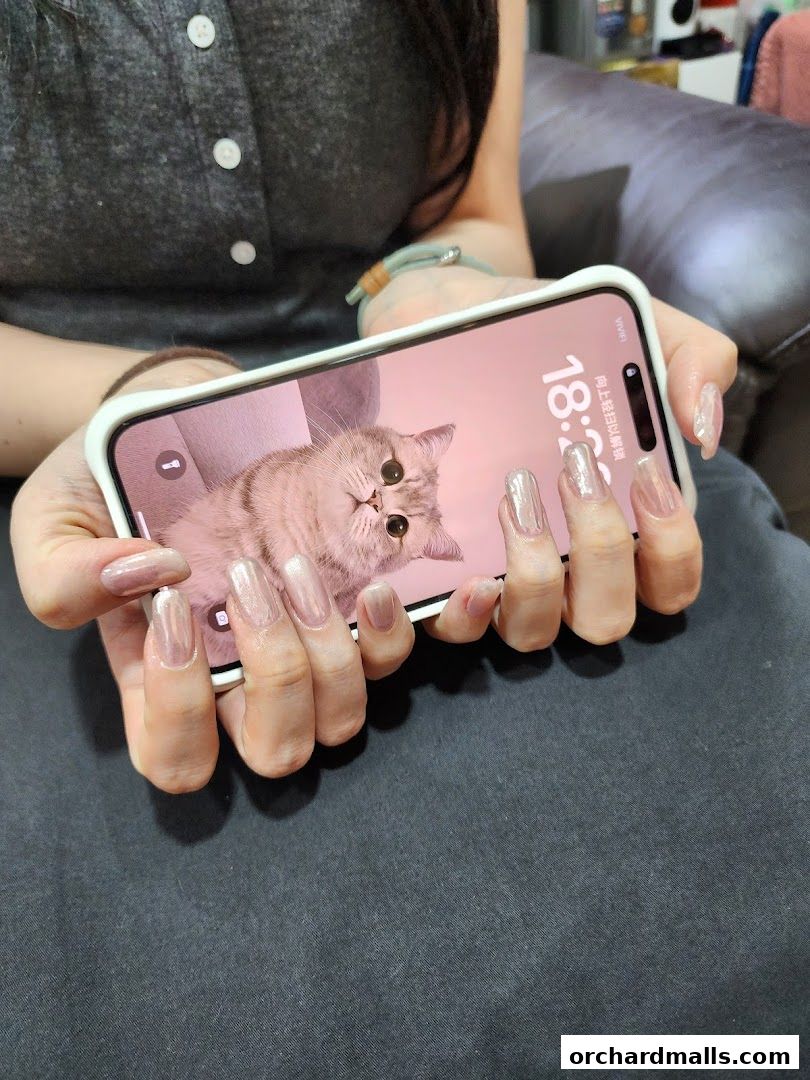A person shows off their new, shimmering nail art while holding a smartphone with a cat wallpaper.