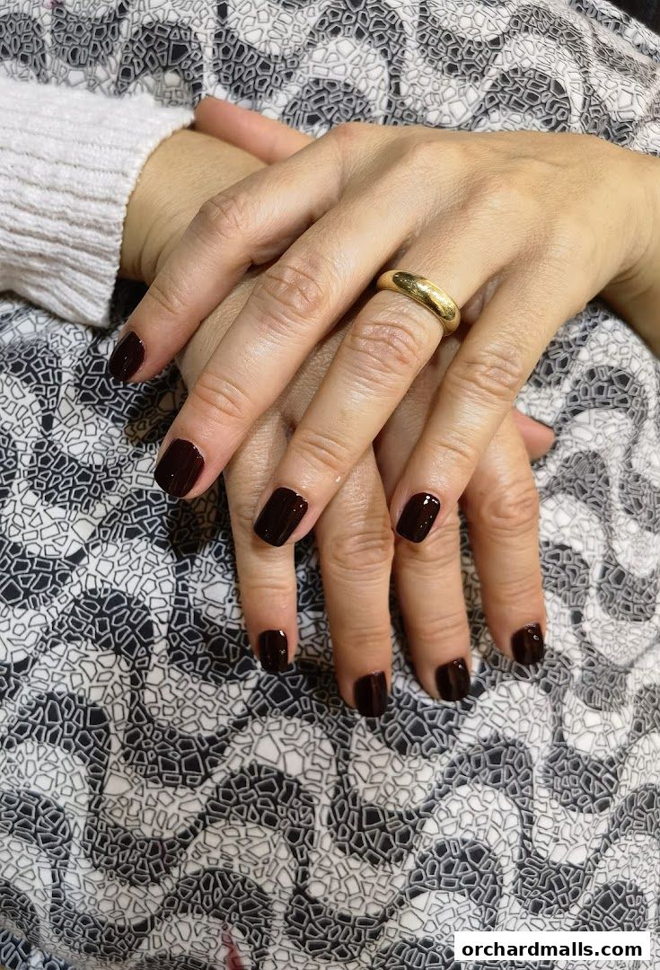 Close-up of hands with dark red polished nails and a gold ring.