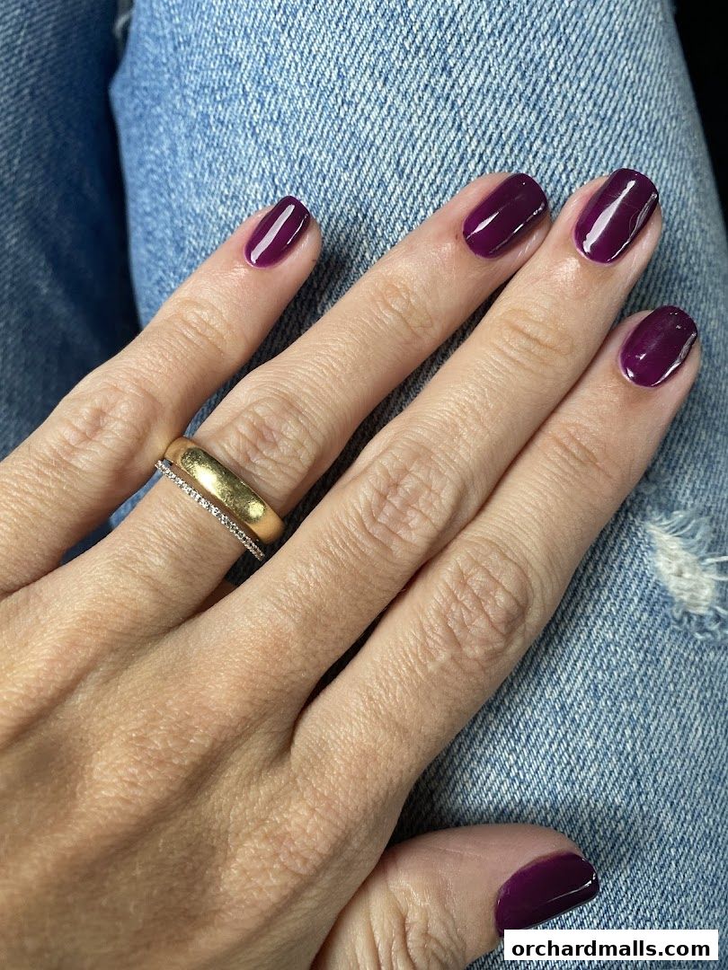 A close-up of a hand with dark purple nail polish and rings.