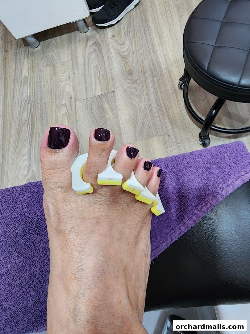 A close-up of a foot with dark nail polish and toe separators, ready for a pedicure.
