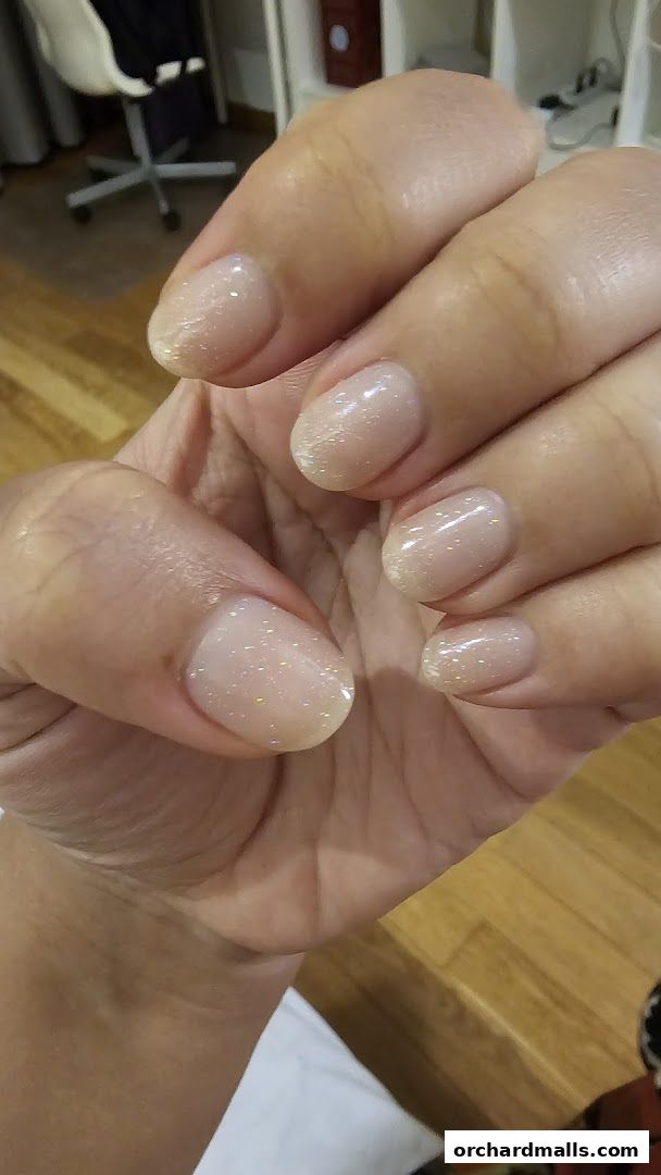Close-up of a hand with perfectly manicured, sparkling nude-toned nails.