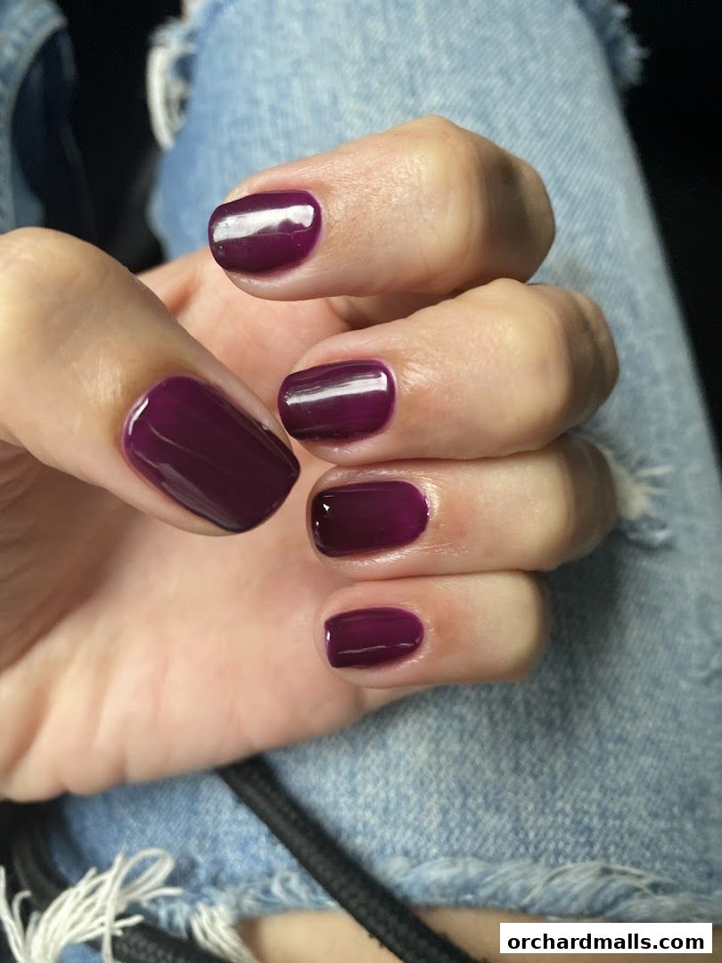Close-up of a hand with perfectly manicured, glossy dark purple nails.