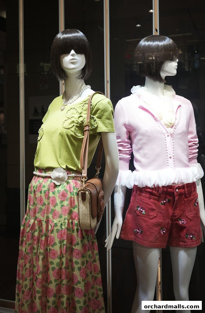 Mannequins display a lime green top with floral embellishments and a rose-print skirt, and a pink cardigan with ruffled shorts.