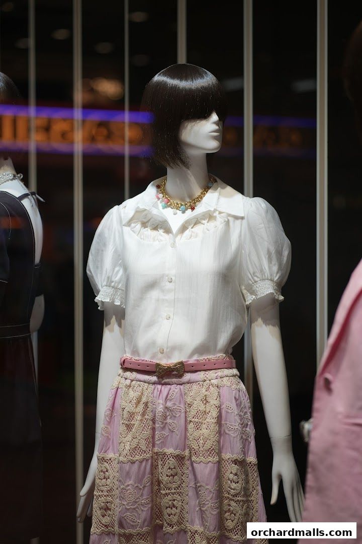 Mannequin displays a white blouse, pink lace skirt, and statement necklace.