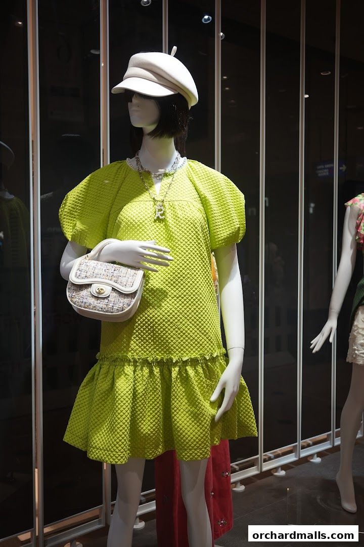 Mannequin in a lime green textured dress, white cap, and handbag in a shop window.