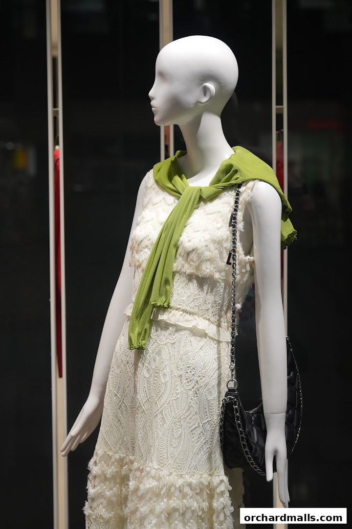 Mannequin in a white lace dress with a green scarf and black handbag.