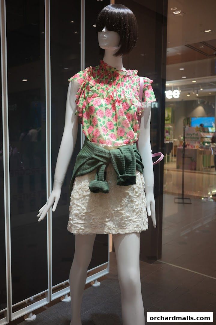 Mannequin in a store window displaying a floral top and textured skirt.