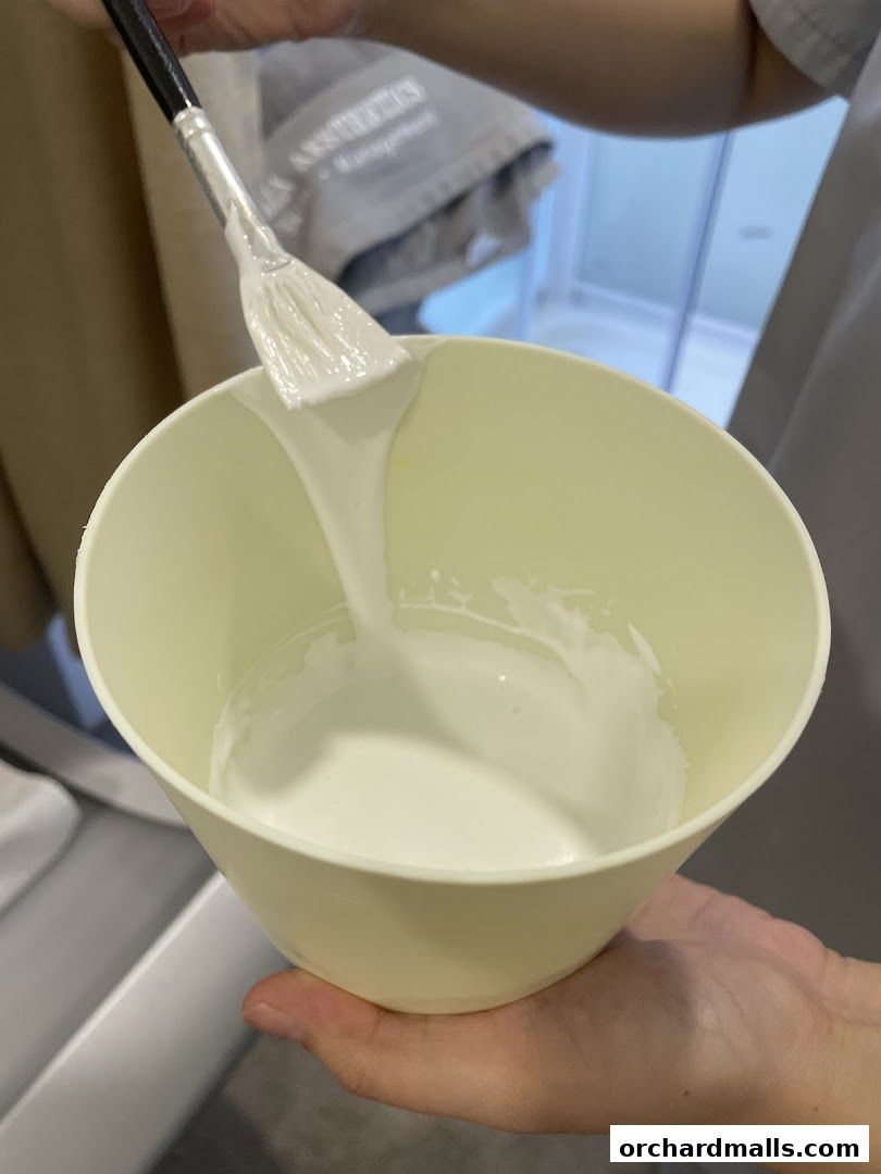 Aesthetician preparing a facial mask with a brush in a bowl.