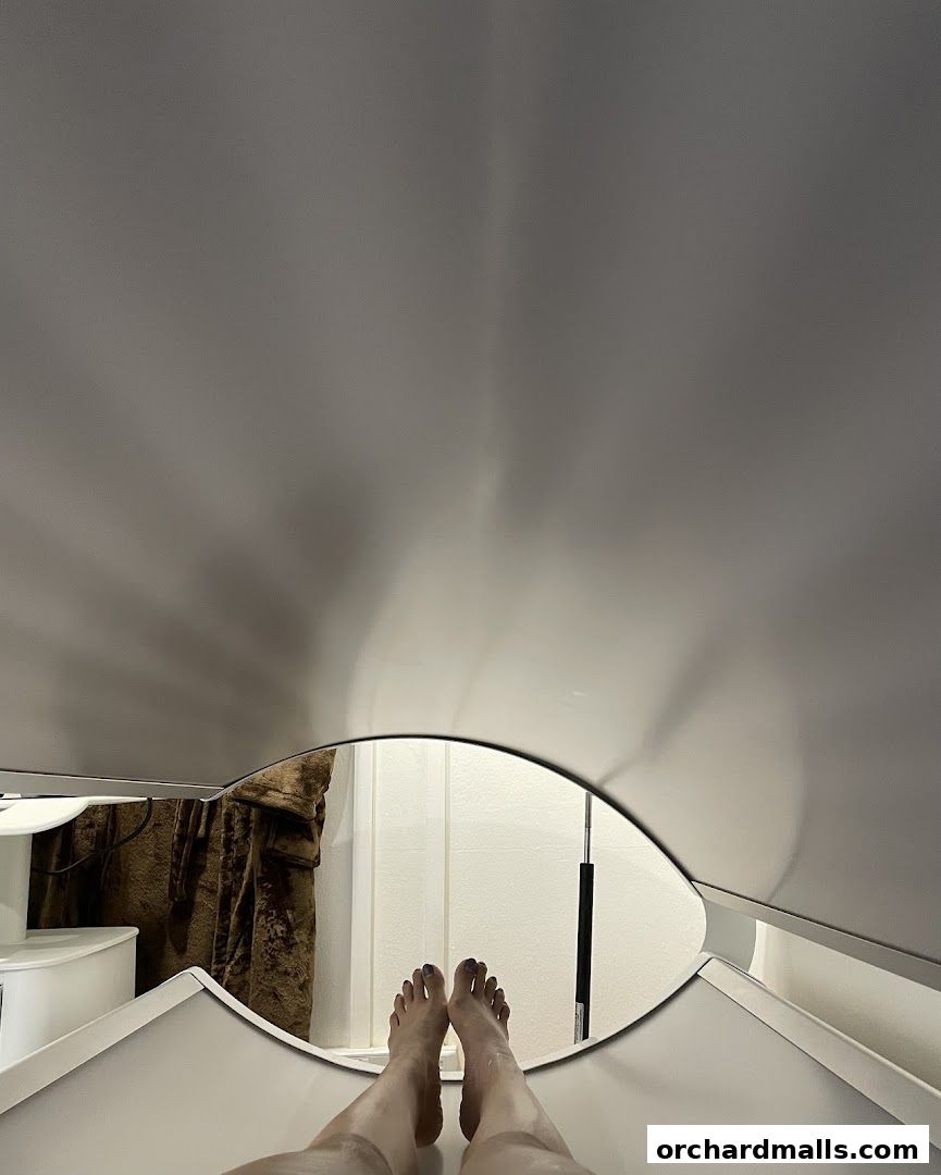 A person's feet are reflected in a mirror in a modern, minimalist room.