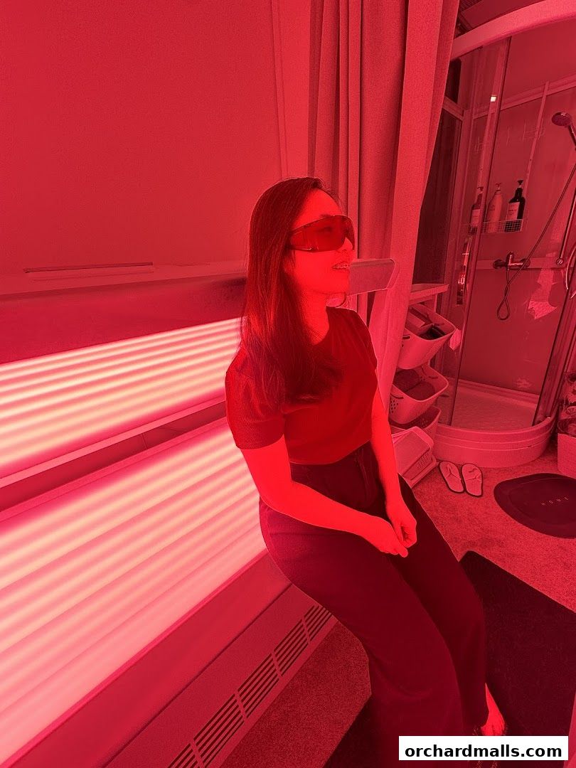Woman wearing red goggles sits in a room with red light therapy equipment.