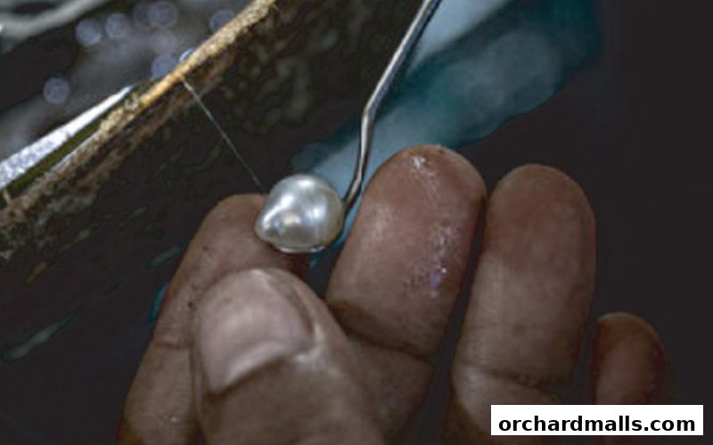 Close-up of a pearl being held by fingers with a tool.