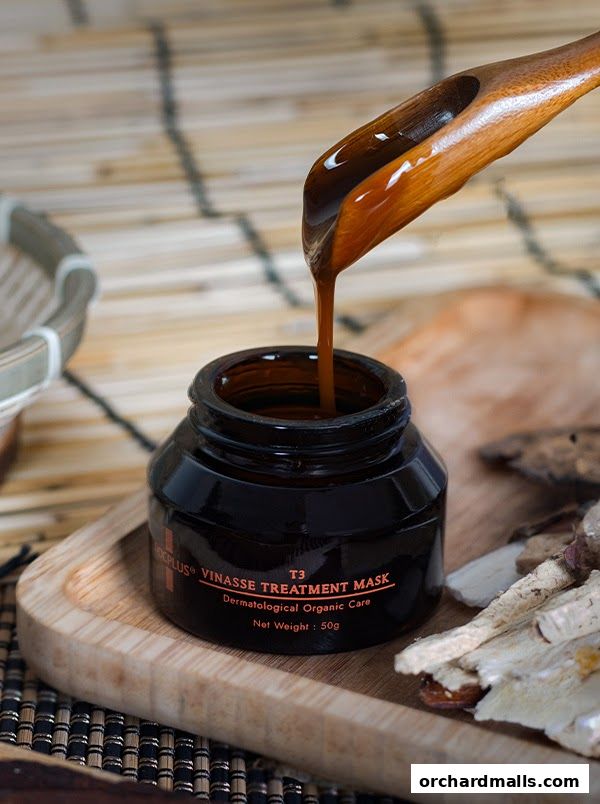 A wooden spoon pours a dark liquid into a jar labeled 'Vinasse Treatment Mask'.