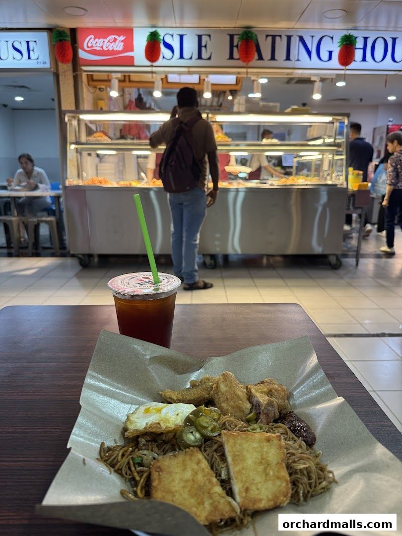 A plate of noodles with fried items and a drink in front of a food stall.