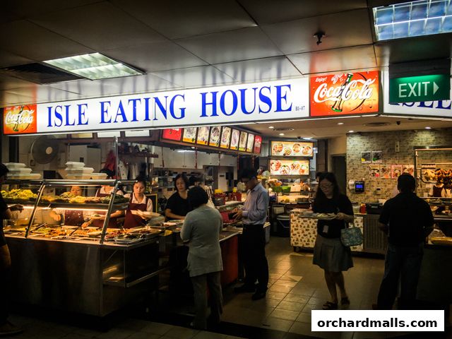 A busy food stall with a variety of dishes displayed and customers being served.