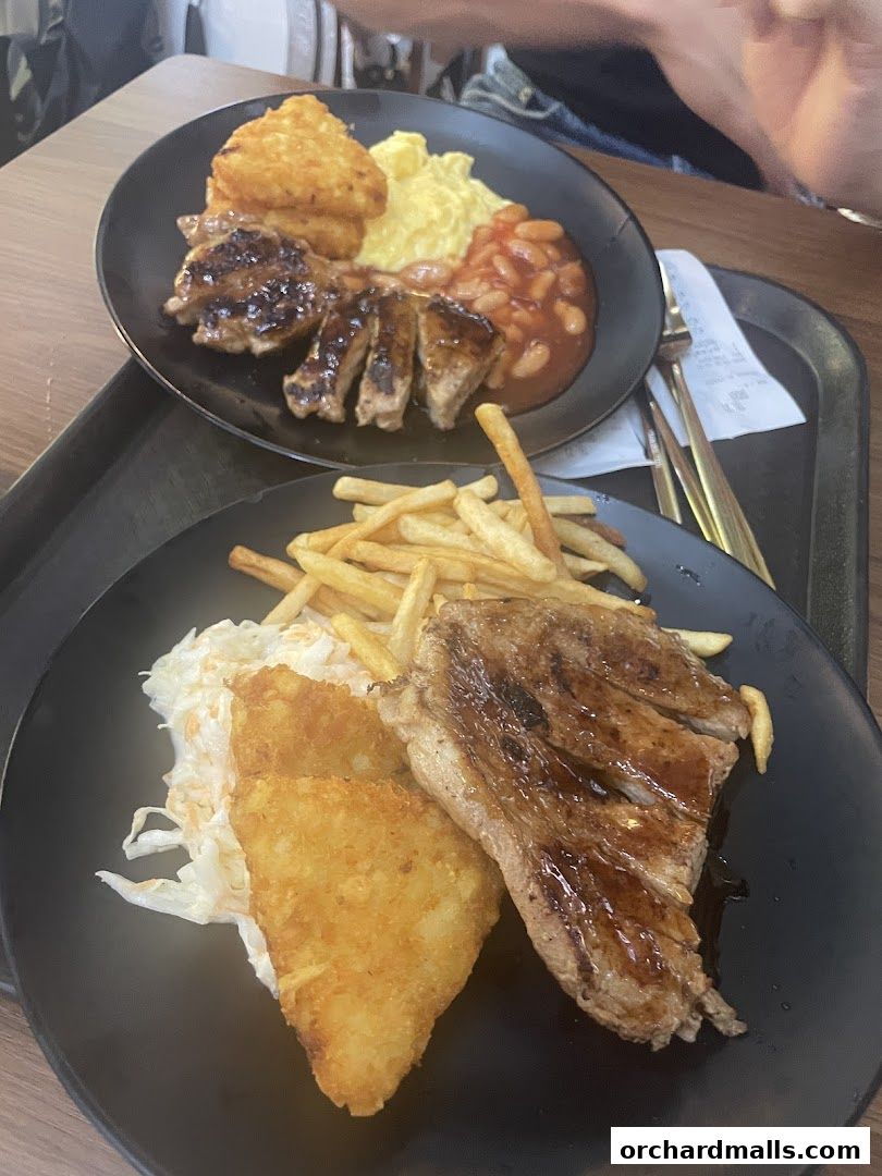 Two plates of hearty meals featuring grilled meat, hash browns, fries, and beans.