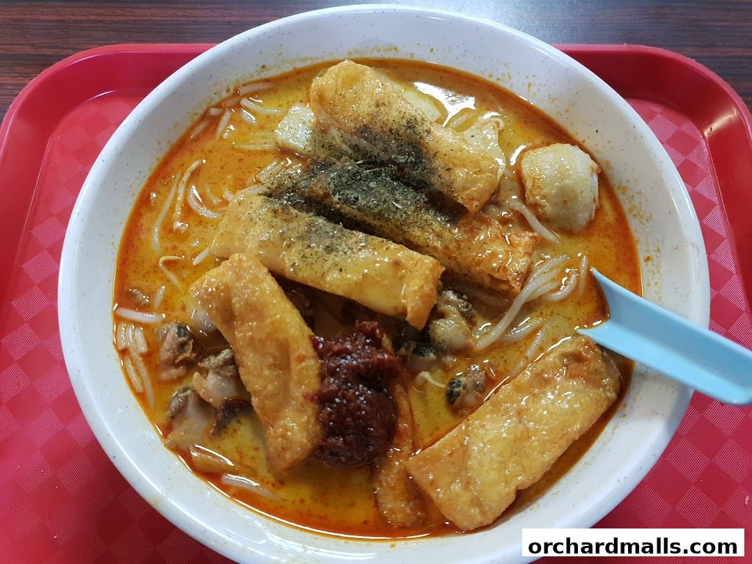 A close-up shot of a delicious bowl of curry laksa with fried tofu, fish balls, and chili paste.