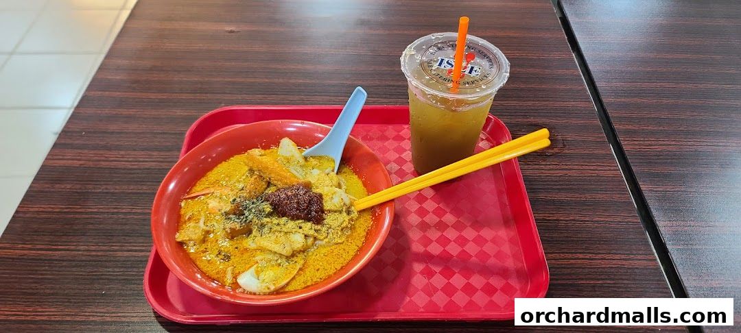 A bowl of laksa and a drink served on a red tray on a wooden table.