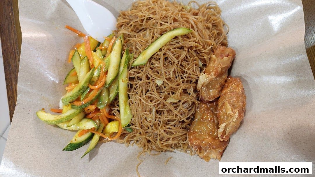 A plate of fried noodles with a side of cucumber and carrot salad and fried tofu skin.