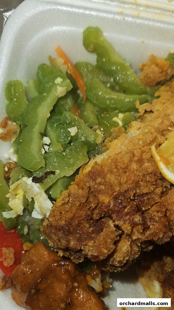 A close-up of a takeout container filled with food, including fried fish and vegetables.