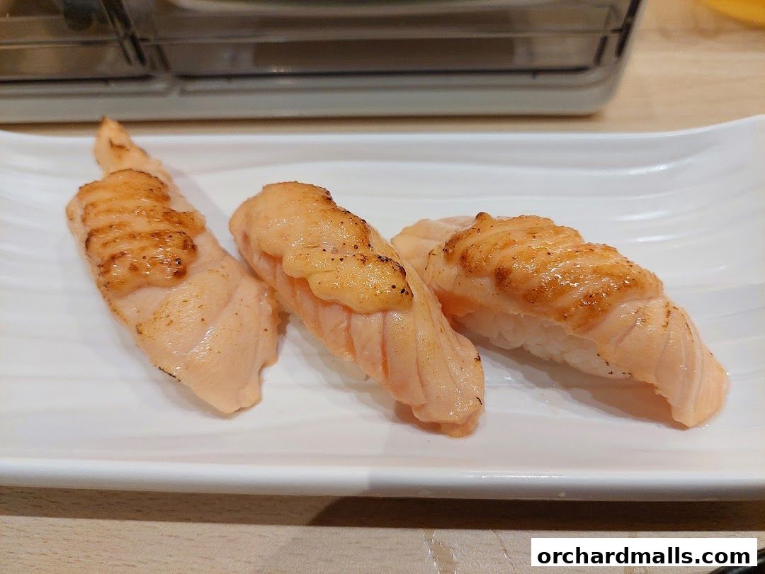 Three pieces of seared salmon sushi on a white plate.