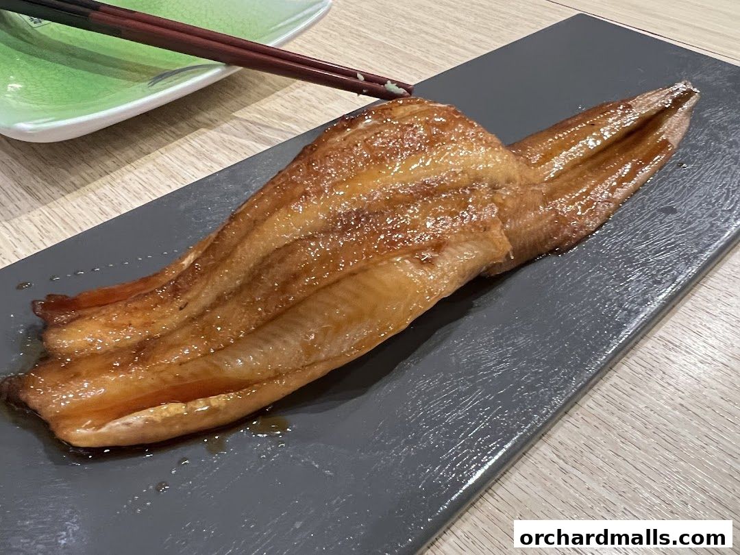A close-up of a glazed eel dish served on a dark rectangular plate with chopsticks.