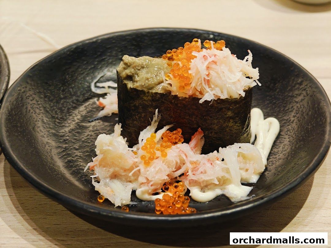 A close-up of a sushi roll with crab meat, roe, and sauce on a black plate.