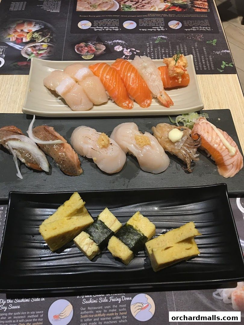 A close-up of various sushi and tamagoyaki dishes served on black and white plates.