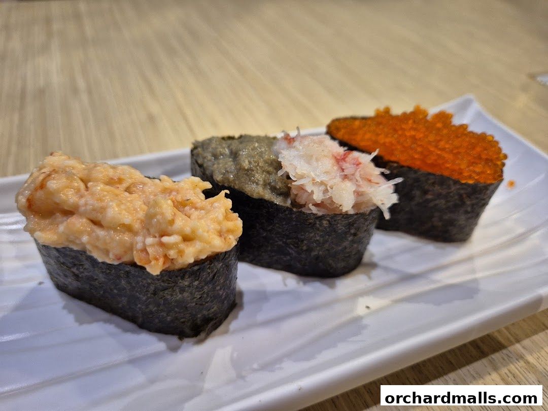 Three gunkan maki sushi pieces with different toppings on a white plate.