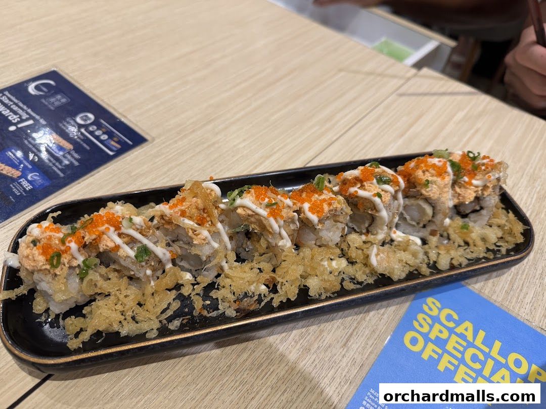 A plate of sushi rolls topped with sauce, roe, and green onions, served with crispy tempura bits.