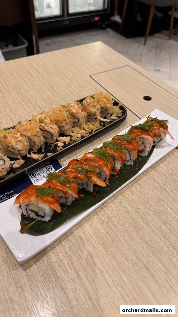 Two plates of sushi rolls, one topped with crispy bits and sauce, the other with a spicy glaze.