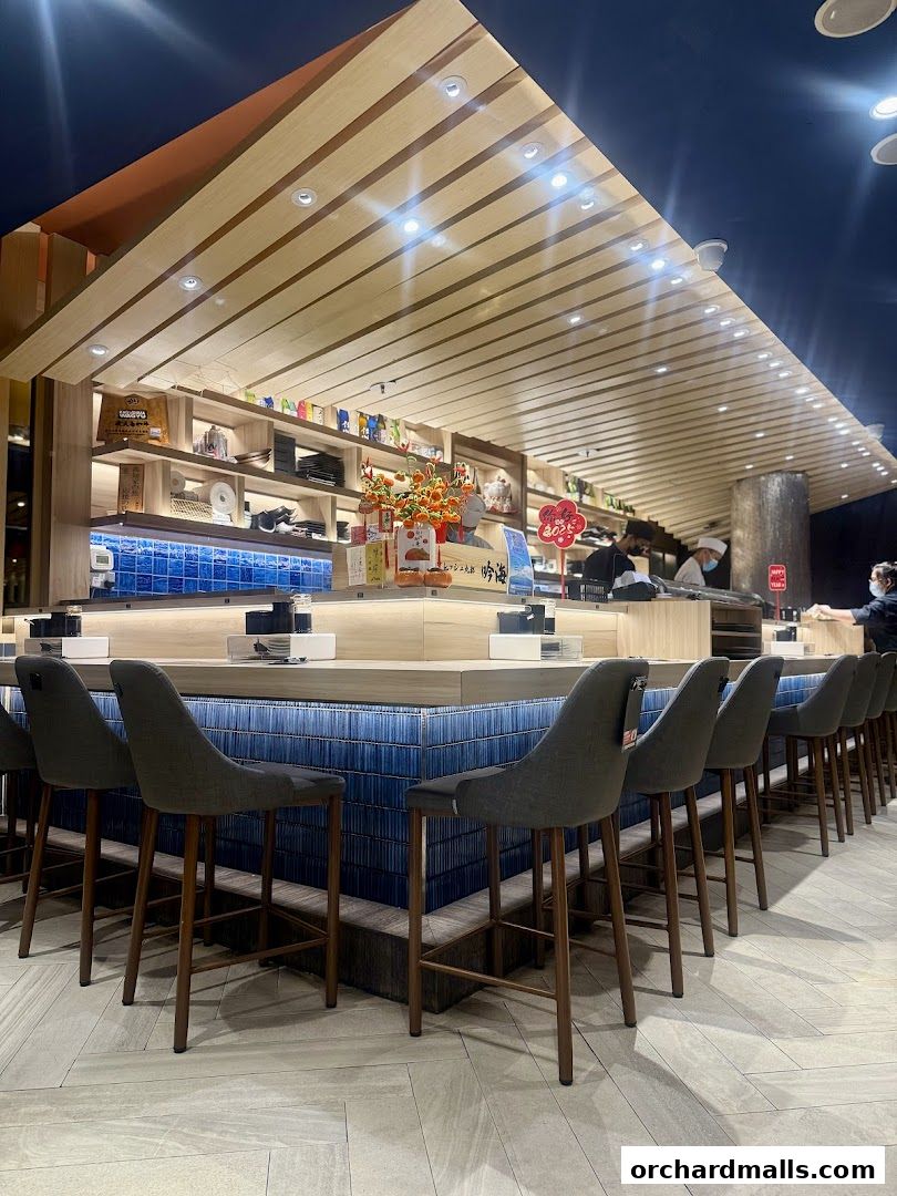 Interior view of a modern sushi bar with counter seating and shelves stocked with products.