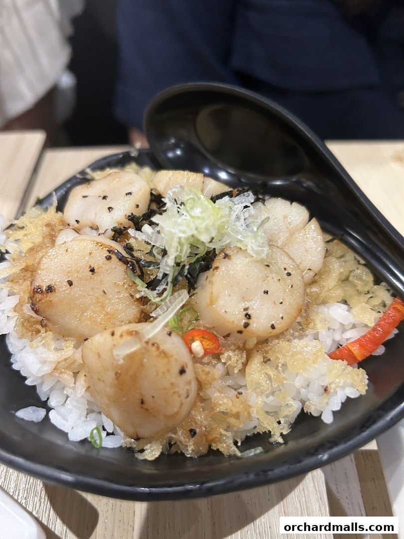 A close-up of a scallop rice bowl with garnishes and a spoon.